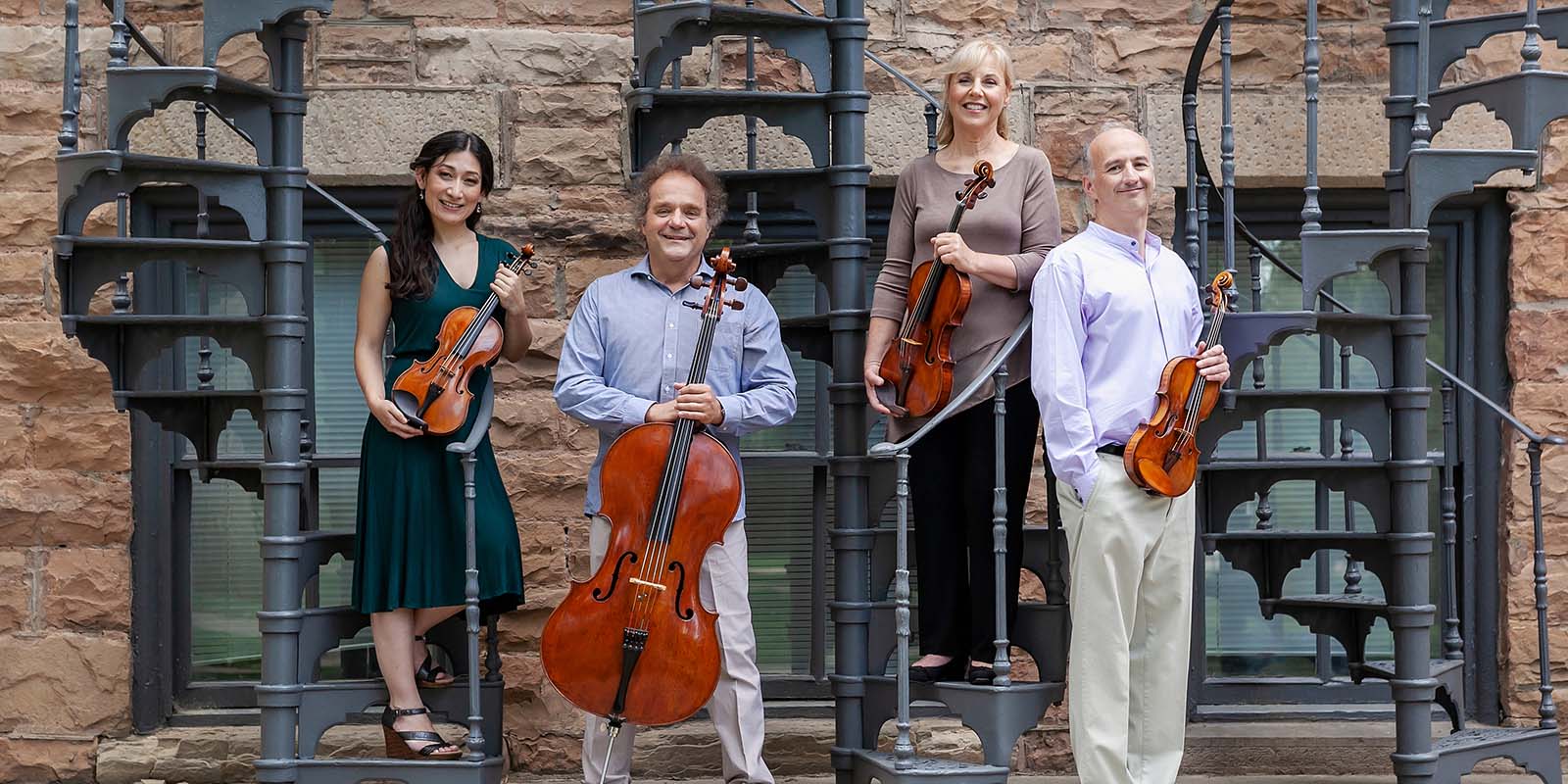 Takacs Quartet posing in front of a brick building with stairs.