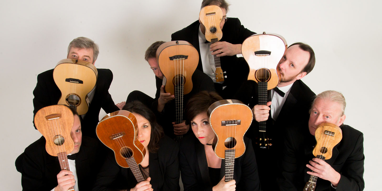 Ukulele Orchestra of Great Britain hiding behind their ukuleles.