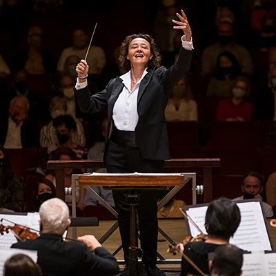 Nathalie Stutzmann stands on a podium with arms extended conducting the Atlanta Symphony Orchestra