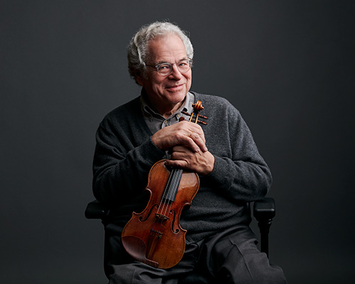 Itzhak Perlman sits holding a violin in front of a dark background