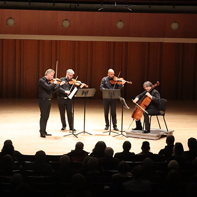 A string quartet performs in front of an audience in a concert hall