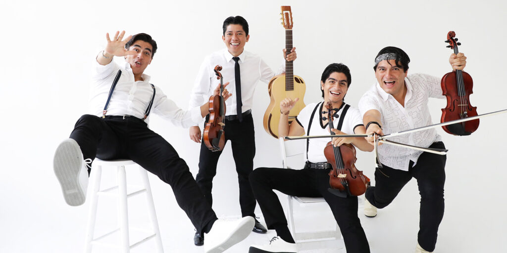 Four men in white shirts and black pants sit in a white room holding violins and a guitar