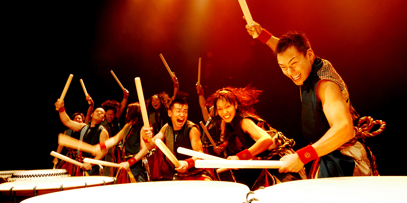 People in hold drumsticks and pound on large drums