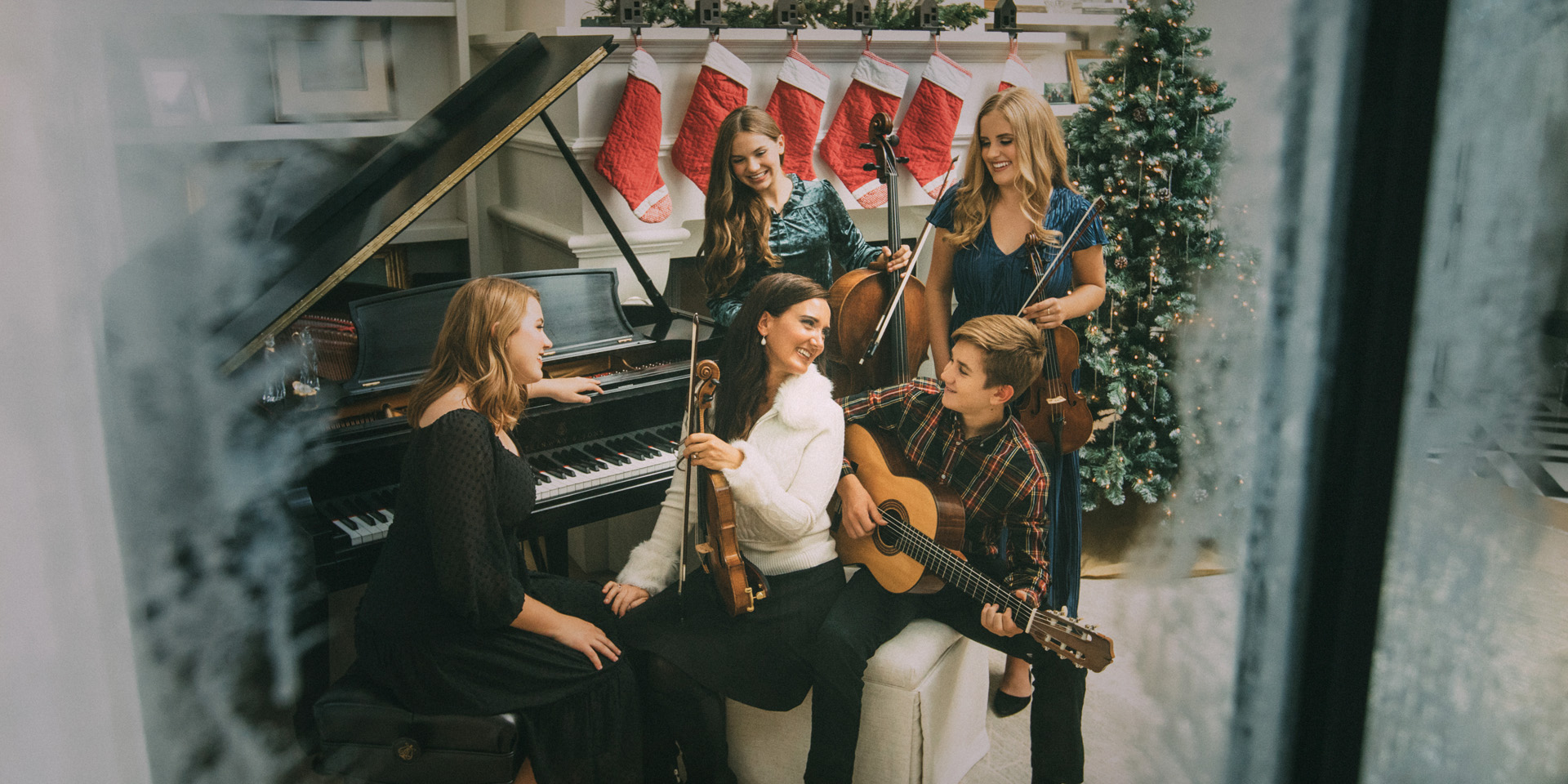 Five people holding string instruments sit at a piano