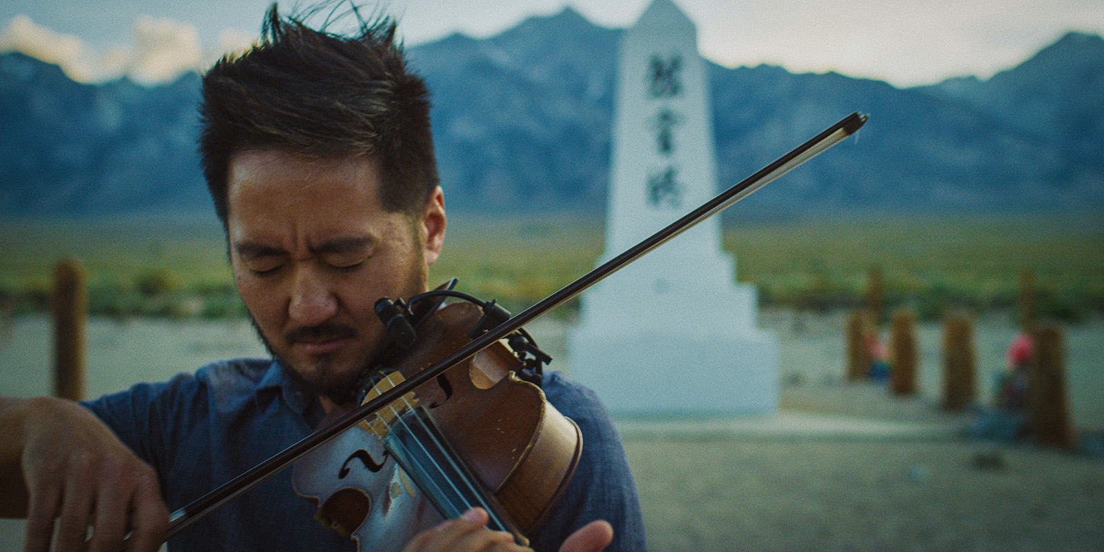 A man plays a violin outside in front of a monument