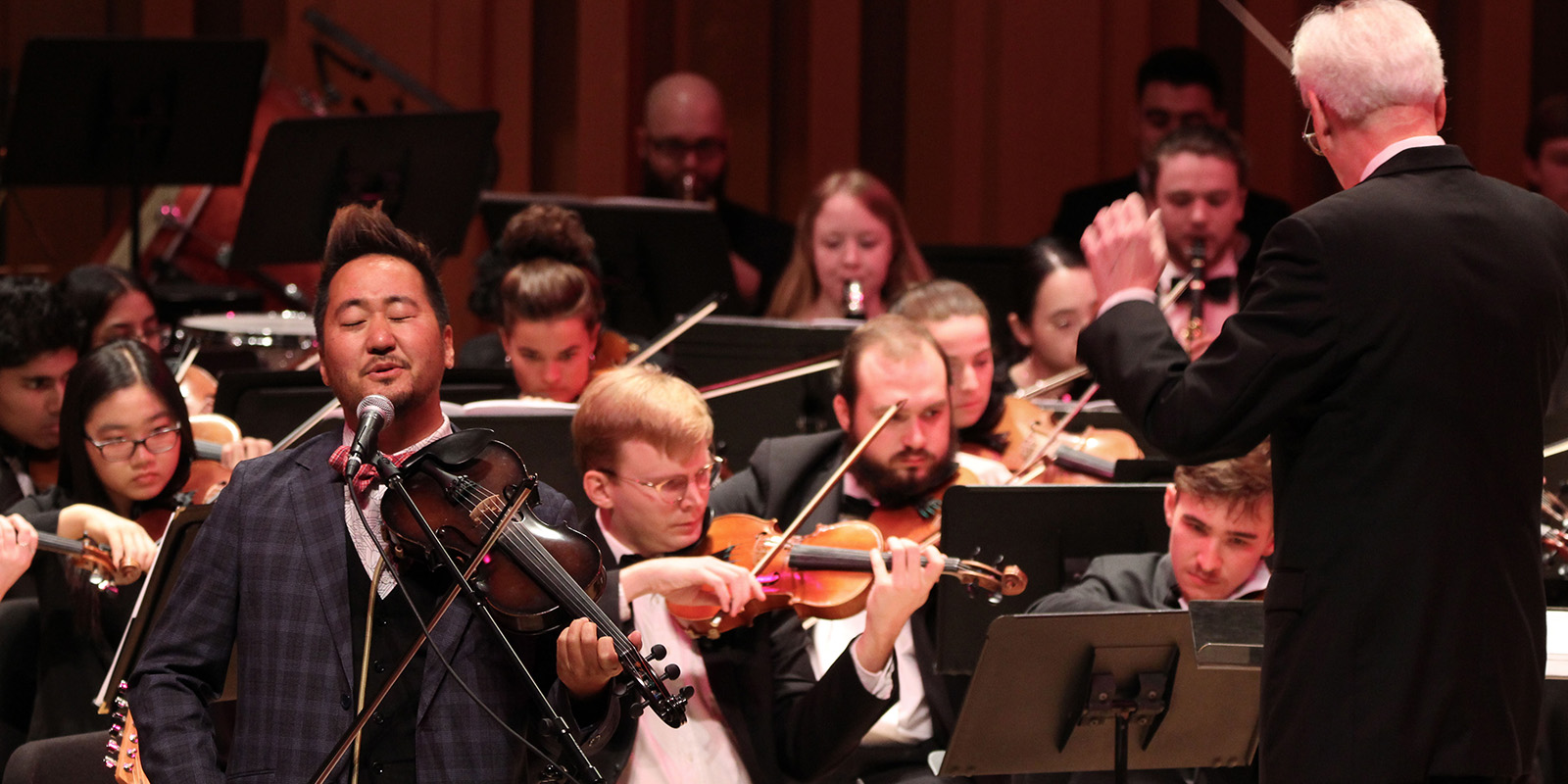 A man plays a violin in front of an orchestra.