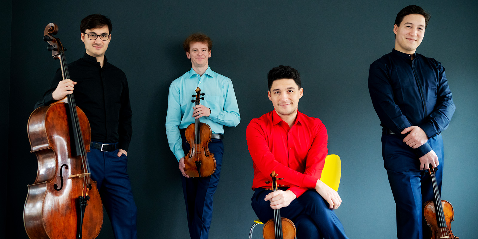Four men wear colorful shirts and hold violins, a viola, and cella