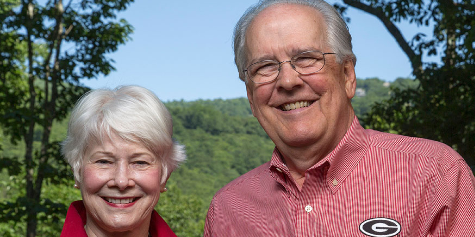 Lynne and Charles Knapp smiling and looking at the camera in front of a green landscape