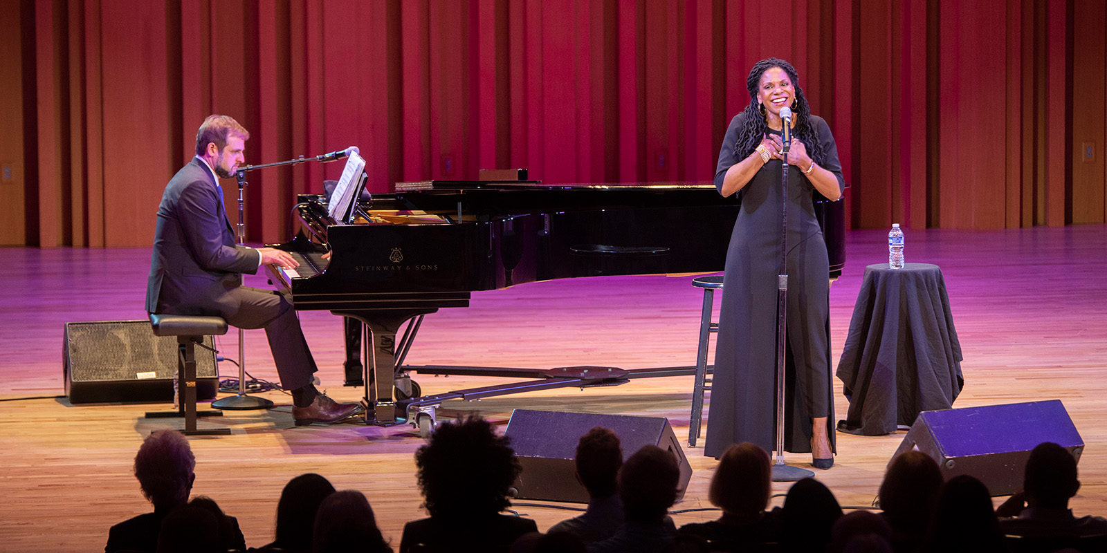 Audra McDonalds stands in front of a black grand piano on Hodgson Concert Hall stage