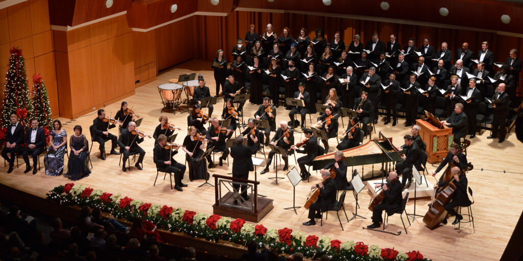 An orchestra and choir wear black formal attire sit on stage.