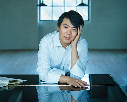 Lang Lang leans over the closed lid of a black grand piano.