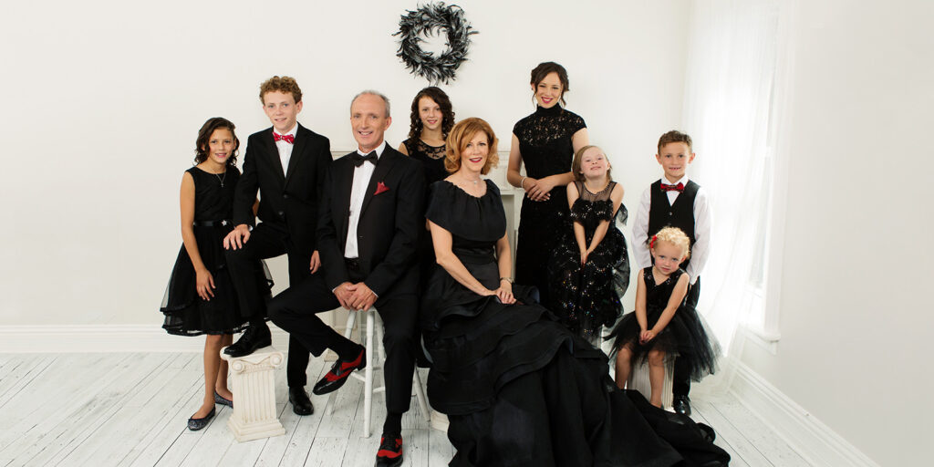The Leahy family, including seven children, sit in a white room wearing formal attire.