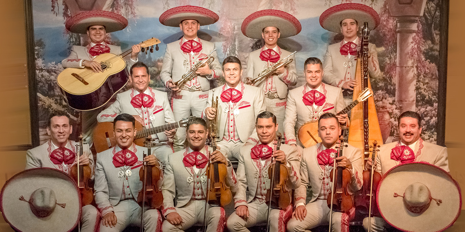 Men in traditional mariachi dress sit in front of a colorful backdrop holding instruments.