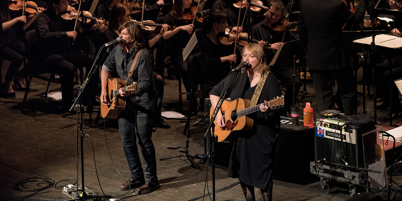 Indigo Girls perform on stage with a large orchestra