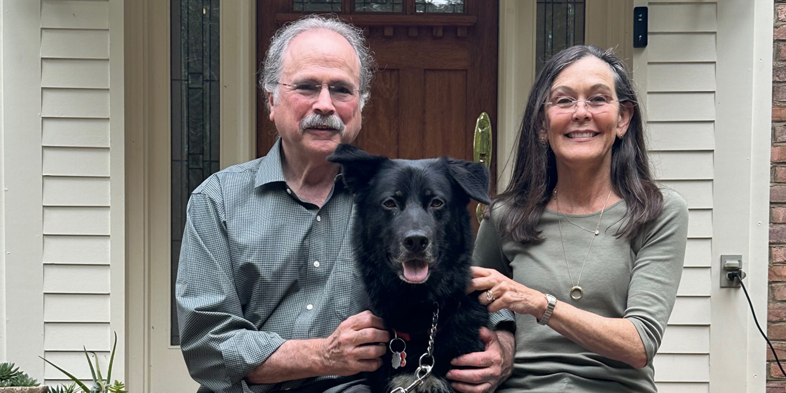 Charlie and Teresa Friedlander sit on a brick step with their black dog.