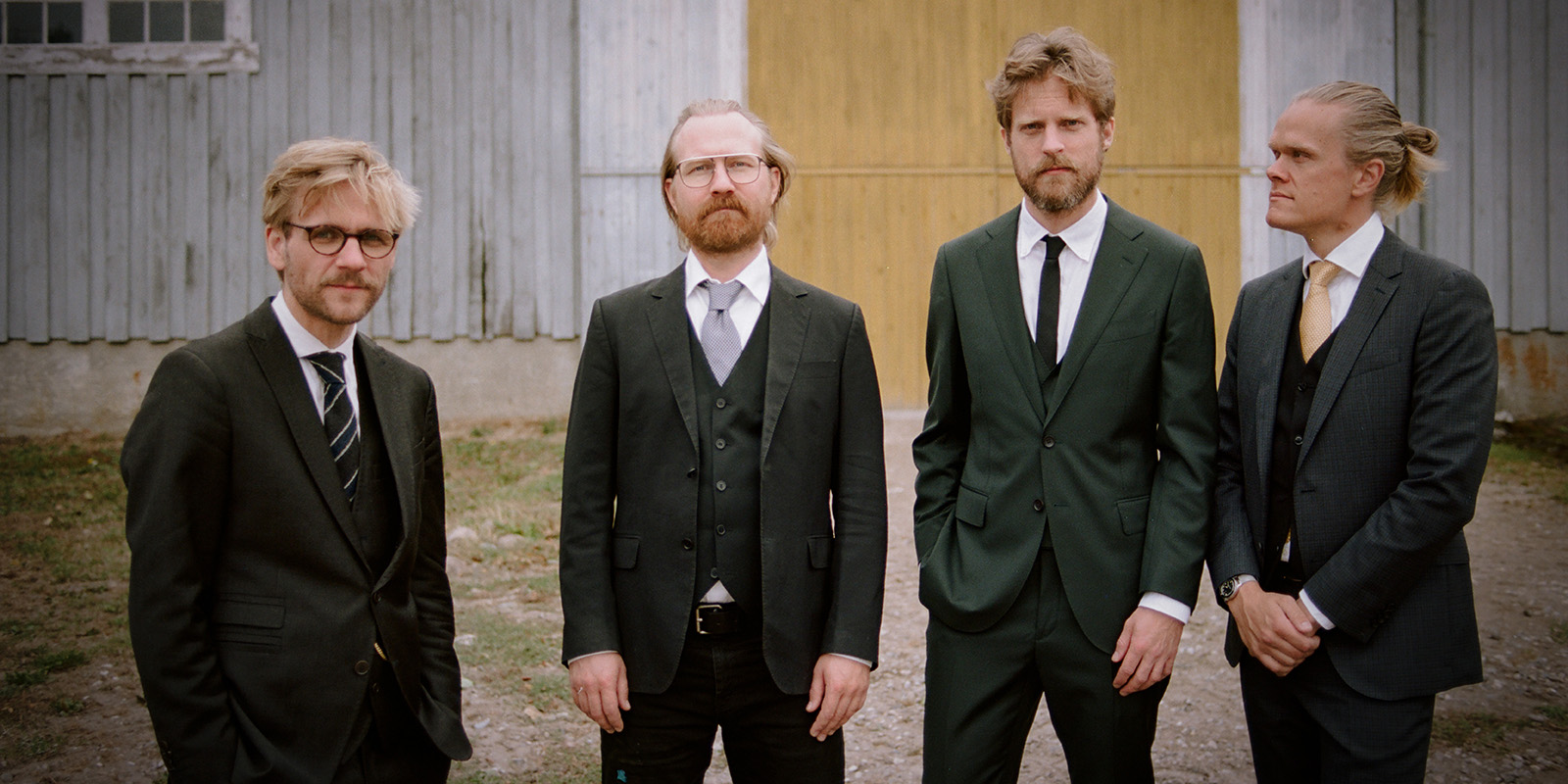 Four men in dark suits standing outdoors.