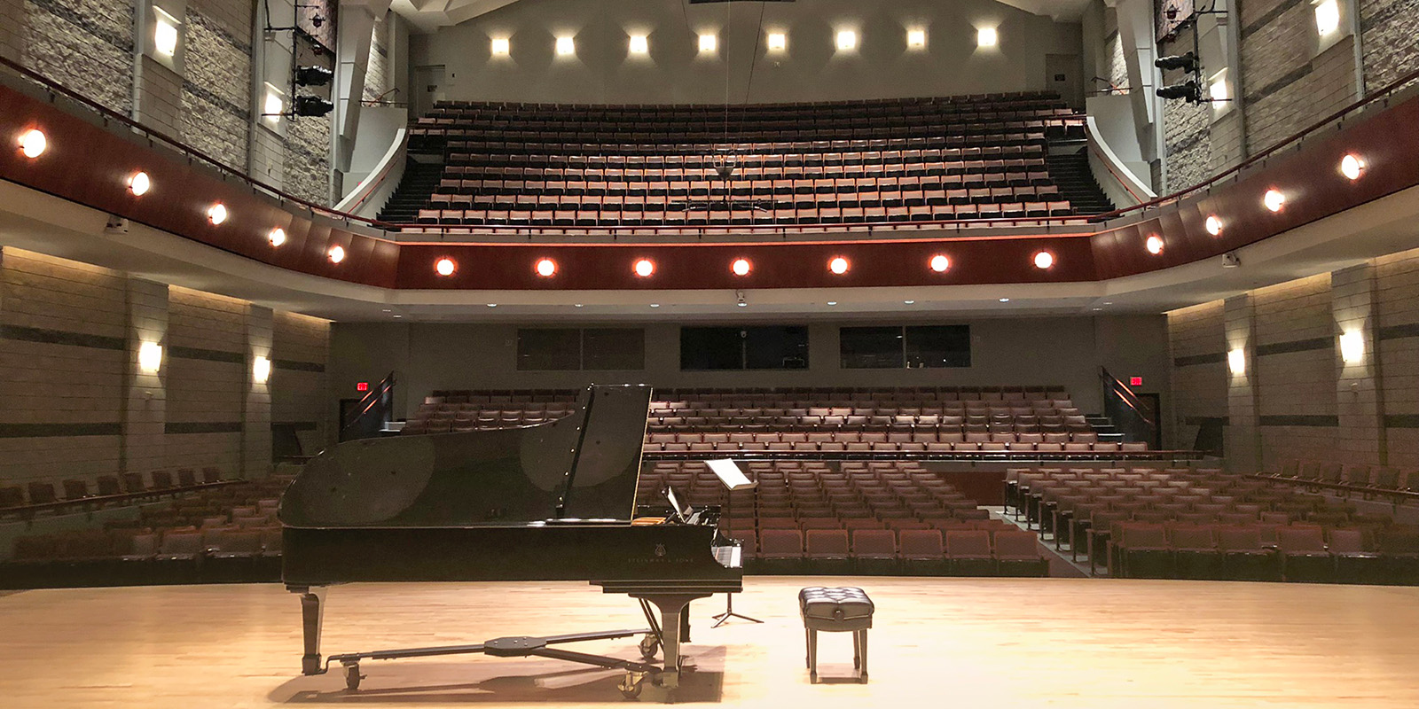 A large black piano sits on a stage in front of an auditorium of empty seats.