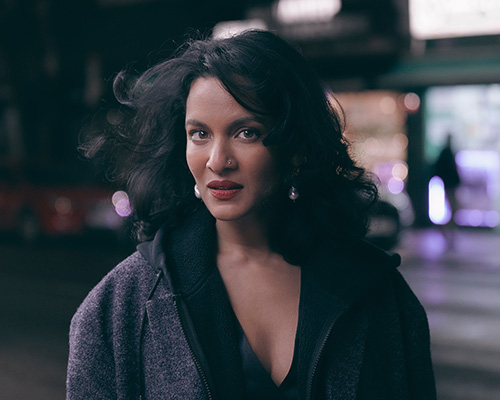 A woman with long dark hair stands on a dark city street.