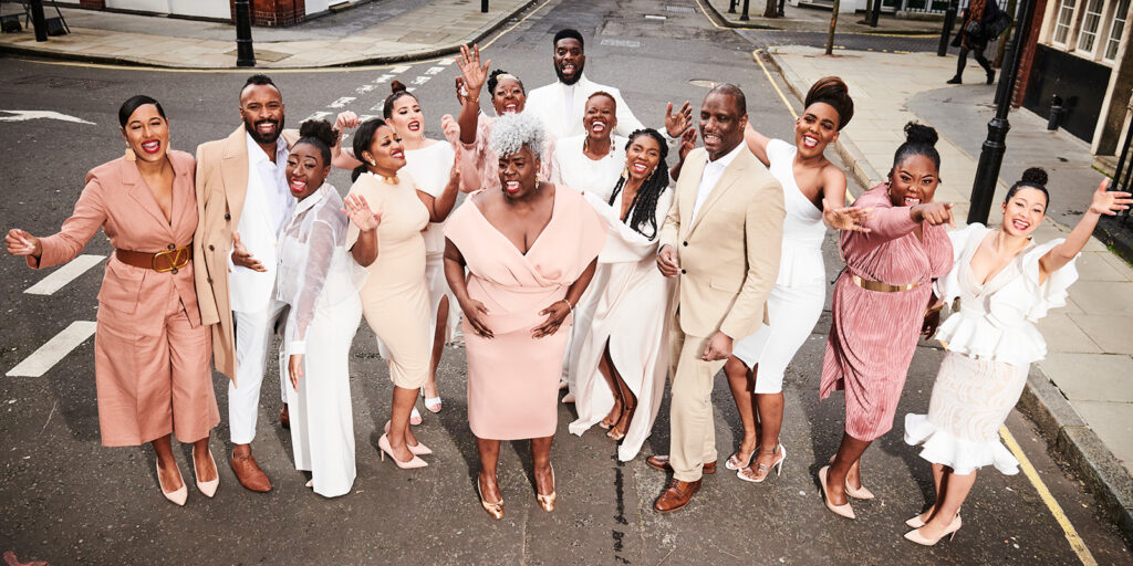 A group of men and women wearing white, pink, and beige clothing stand in the middle of an empty street.