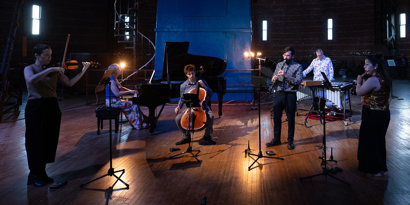 Six musicians plays various instruments in a dark warehouse.