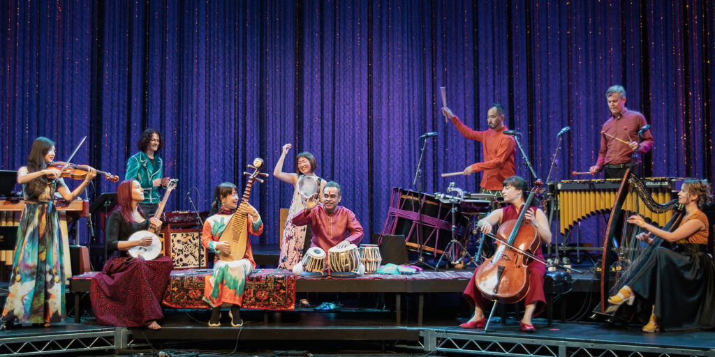 A group of musicians sit on a stage with a variety of traditional instruments.