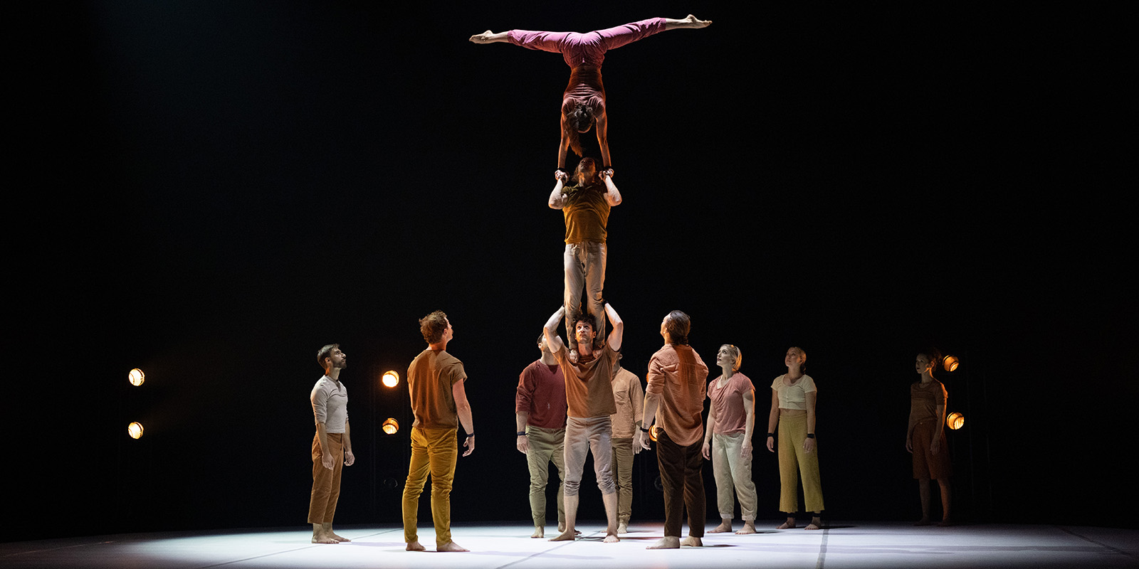 Acrobats stand on a stage as two acrobats stand on a man's shoulders.