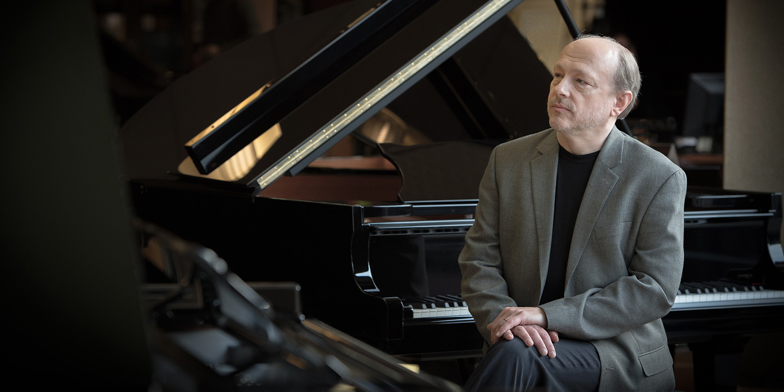 A man in a gray suit sits at a black piano.