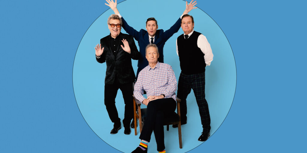 Three smiling men stand and one man sits in front of a blue background