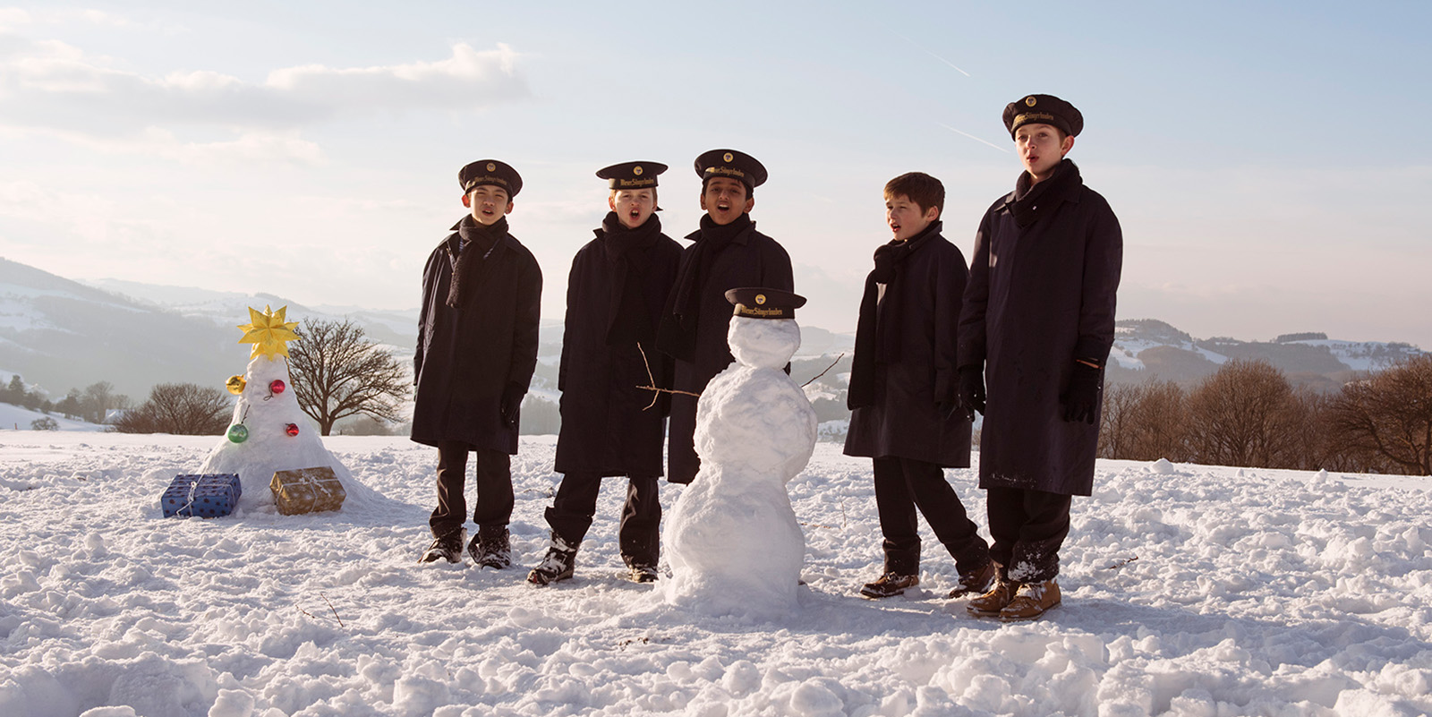 Boys in dark coats and hats play in the snow and build a snowman.