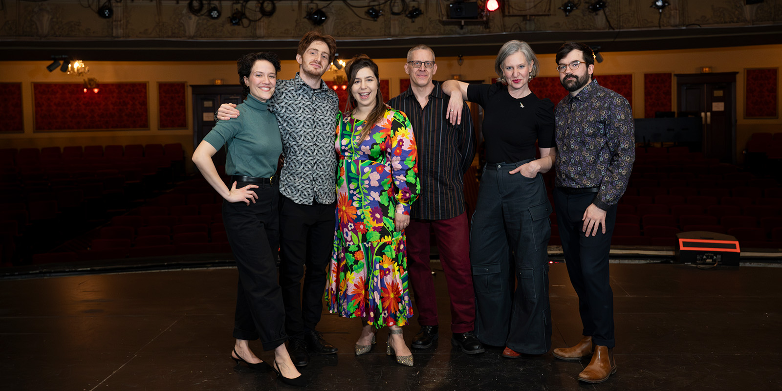 A group of musicians stand on a bare stage.