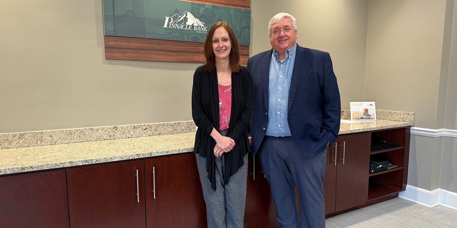 A woman and a man in dark jackets stand in from of a Pinnacle Bank sign.