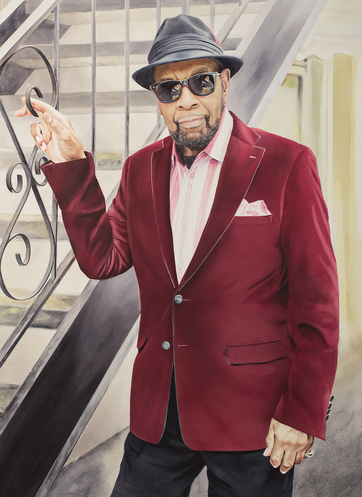 A stylish older man wearing a maroon velvet blazer, pink shirt, black hat, and sunglasses stands by a wrought iron staircase, leaning casually and smiling at the camera.