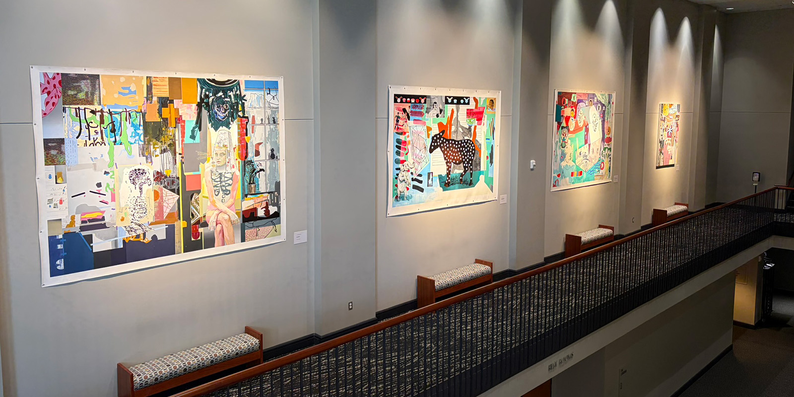 Four colorful abstract paintings hang on a grey wall in a well-lit gallery space above a corridor with patterned carpeting and benches beneath each artwork. The area is illuminated by spotlights from above.
